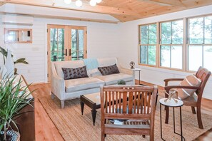 A cozy living room with a sofa, wooden chairs, a coffee table, and a large window. - Updated 3BR Lakefront Dog Friendly - Washer Dryer (Moultonborough)