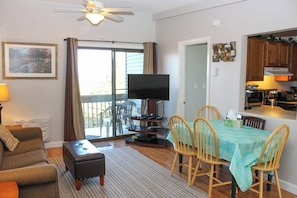 A living room with a sofa, a coffee table, a television, and a dining area with a table and chairs. - 3BR Near Golf - Balcony - Pool - Tennis Courts (Laconia)