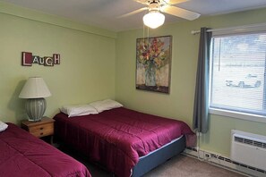 A bedroom with two beds, a ceiling fan, a lamp, a painting, and a window with blinds. - 3BR Near Golf - Balcony - Pool - Tennis Courts (Laconia)