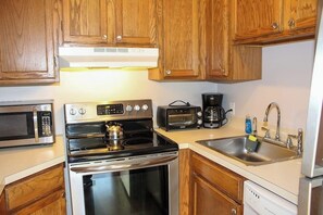A kitchen with wooden cabinets, a microwave, a stove, a toaster, a coffee maker, and a dishwasher. - 3BR Near Golf - Balcony - Pool - Tennis Courts (Laconia)