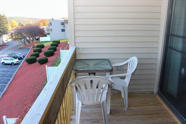 A balcony with a table and chairs, a red carpet, and a view of parked cars and trees. - 3BR Near Golf - Balcony - Pool - Tennis Courts (Laconia)