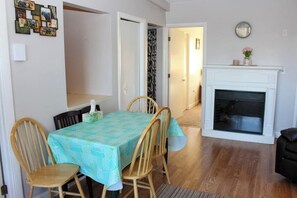 A dining area with a table set for four, wooden chairs, a white fireplace, and a wall with framed pictures. - 3BR Near Golf - Balcony - Pool - Tennis Courts (Laconia)