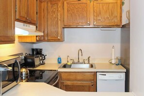 A compact kitchen with wooden cabinets, a built-in oven, a coffee maker, a sink, and a dishwasher. - 3BR Near Golf - Balcony - Pool - Tennis Courts (Laconia)
