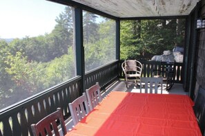A covered outdoor seating area with a table and chairs, overlooking a forested landscape.