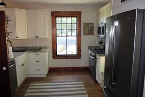 A kitchen with white cabinets, a stainless steel refrigerator, a window with a view, and a striped rug.