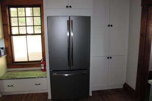 A kitchen with a stainless steel refrigerator, wooden cabinets, and a window with a view.