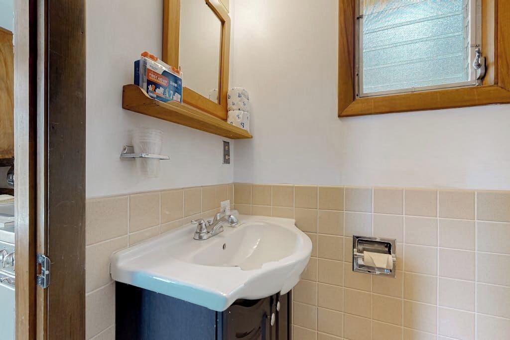 Une salle de bain avec un lavabo blanc, un miroir et une fenêtre avec des stores.