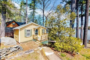A cabin with a porch, surrounded by trees and a body of water.