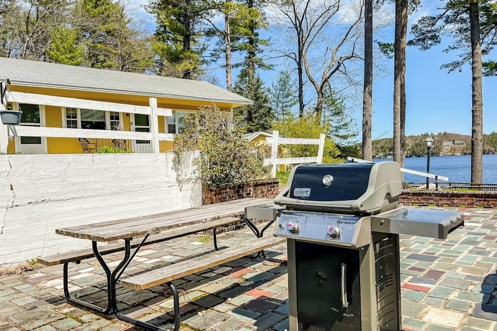 An outdoor patio with a grill, a bench, and a view of a lake.