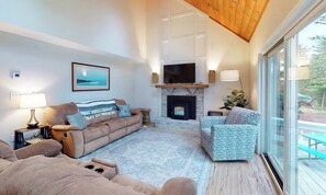 Una sala de estar moderna con chimenea, un televisor grande y vistas al exterior a través de amplias ventanas.