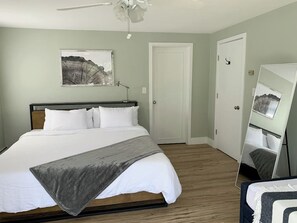 Un dormitorio con cama, mesita de noche, espejo y puerta.