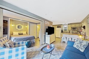 A modern hotel room with a bed, a sofa, a small table, and a kitchenette.