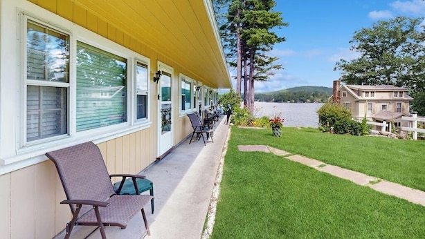 A hotel with a covered outdoor seating area, a grassy lawn, and a view of a body of water.
