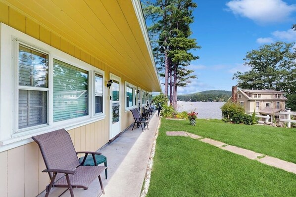 A hotel with a covered outdoor seating area, a grassy lawn, and a view of a body of water.