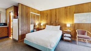 A hotel room with a large bed, a wooden wardrobe, a desk with a computer, and a chair.