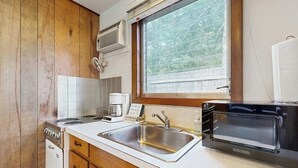 A compact kitchen with a sink, stove, microwave, and window overlooking greenery.