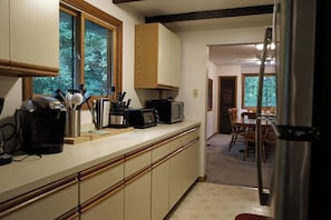 Eine Küche mit Mikrowelle, Toaster und Kaffeemaschine auf der Arbeitsfläche, Holzausstattung und Blick in den Essbereich durch eine offene Tür.
