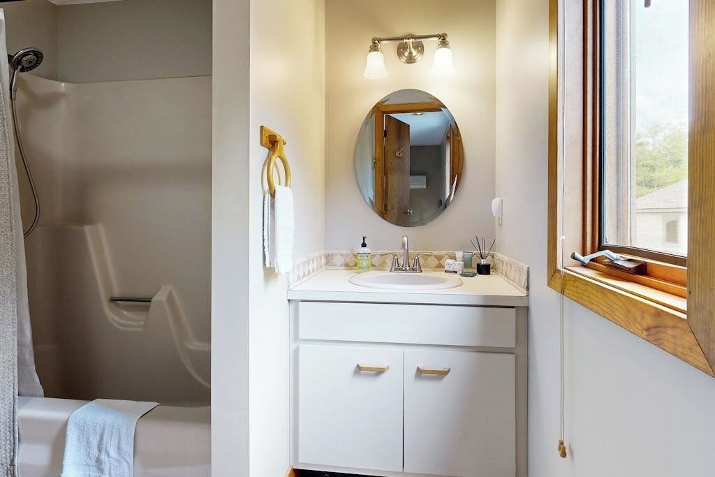 A bathroom with a shower, a sink with a mirror, and a window.