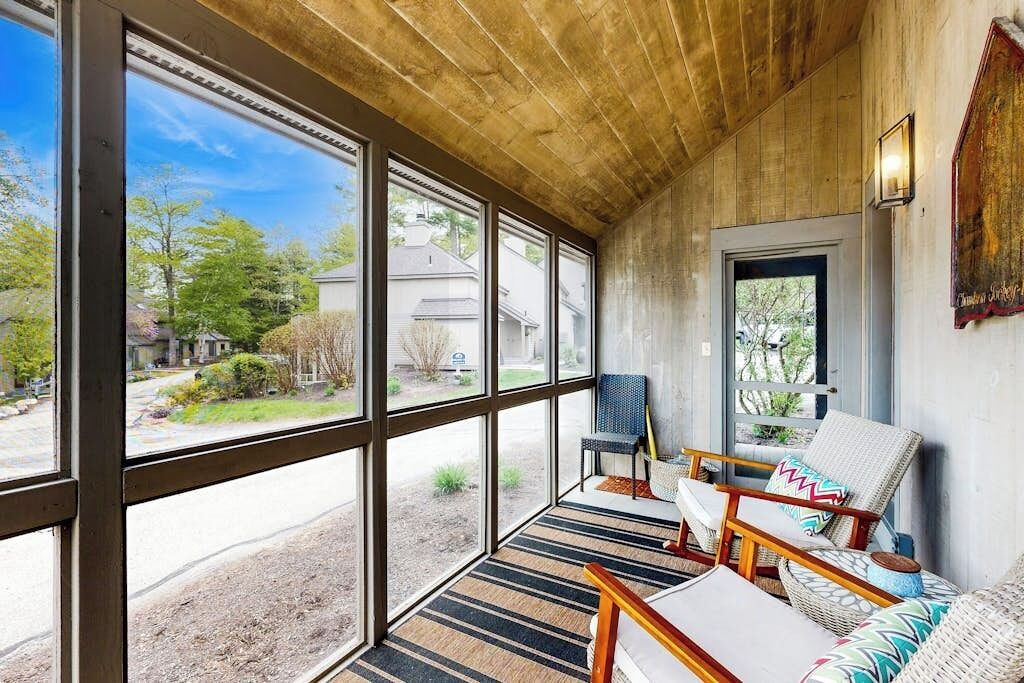 A covered porch with large windows, wicker furniture, and a view of a residential area.