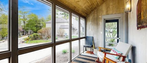 A covered porch with large windows, wicker furniture, and a view of a residential area.