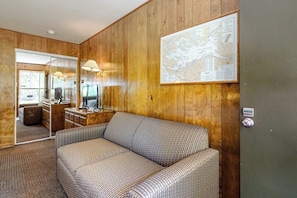 A room with a wooden paneled wall, a sofa, a desk with a computer, and a map on the wall.