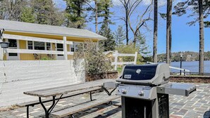 Ein Picknicktisch und ein Weber Spirit Grill in einer Außenanlage mit Blick auf einen See und ein Gebäude im Hintergrund.