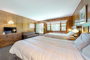 A room with two beds, a television, a sofa, and wooden paneling.