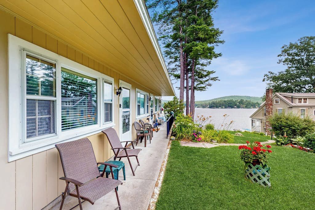 A hotel with a covered outdoor seating area, a view of a lake, and a well-maintained lawn.