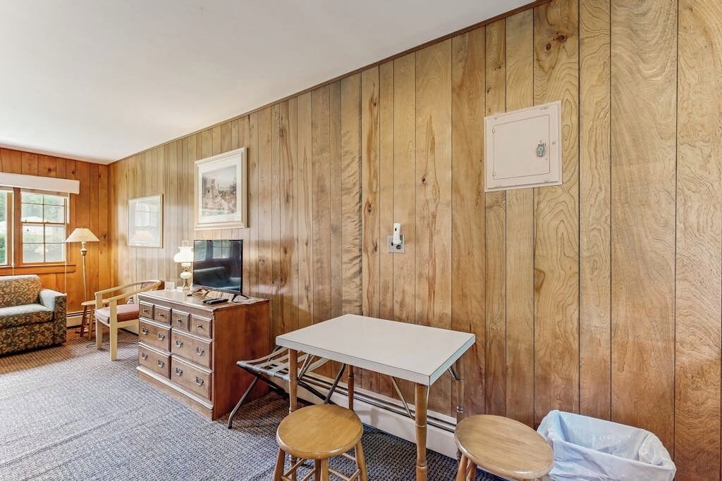 Ein Zimmer mit Holzwandverkleidung, einem weißen Tisch, einem Fernseher, einem Sofa und einem Schminktisch.
