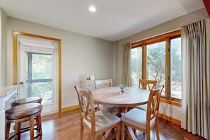 A dining area with a round table and chairs, a window with curtains, and a door with a window view. - 2BR condo with pool and tennis (Gilford)