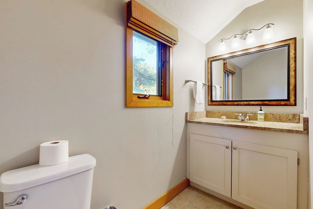 Un bagno con un WC, una finestra con persiana, uno specchio con luci e un lavabo con piano di appoggio.