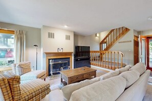 A living room with a fireplace, sofa, and a staircase leading to another level. - 2BR condo with pool and tennis (Gilford)