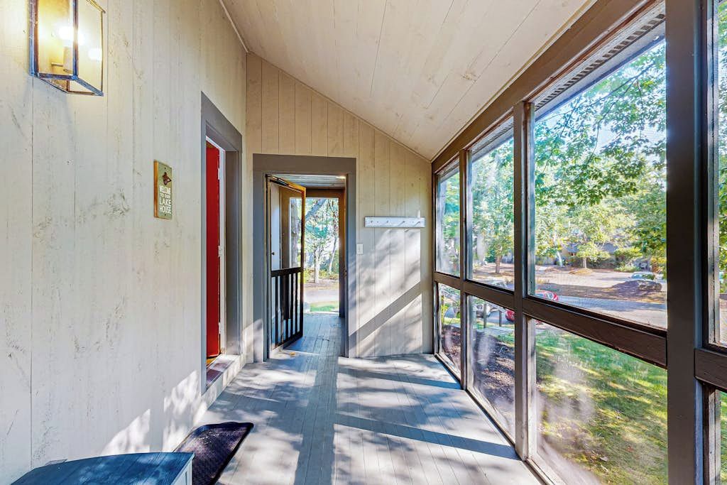 A corridor with wooden walls, a red door, and large windows offering a view of trees and a road.