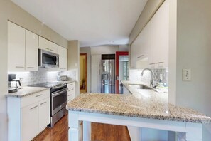 A modern kitchen with a granite countertop, stainless steel appliances, and white cabinetry. - 2BR condo with pool and tennis (Gilford)