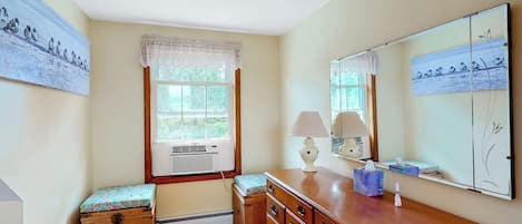 A room with a wooden dresser, a bench, a window with a lace curtain, and wall-mounted artwork.