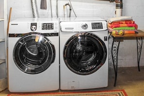 Two front-loading washing machines in a laundry area with a table holding folded laundry and a metal stand. - Updated 3BR Dog Friendly - Deck - Garage Parking (Gilford)