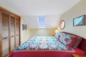 A bedroom with a skylight, a bed with a patterned quilt, wooden closet doors, and a wall-mounted picture. - Updated 3BR Dog Friendly - Deck - Garage Parking (Gilford)