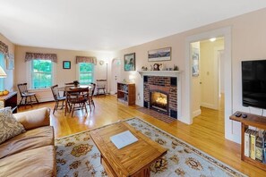 A living room with a fireplace, a television, and a dining area with chairs and a table. - Updated 3BR Dog Friendly - Deck - Garage Parking (Gilford)