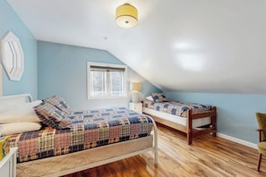 A bedroom with two beds, a window, and a lamp.