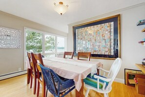 Un coin repas avec une table dressée pour quatre personnes, entourée de chaises, une grande fenêtre offrant une vue dégagée et un luminaire au plafond.