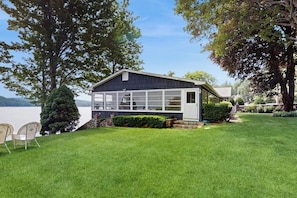 A house with a large windowed front, a lawn, and trees. - 6BR lakefront with deck, dock, lawn & encl porch (Alton)
