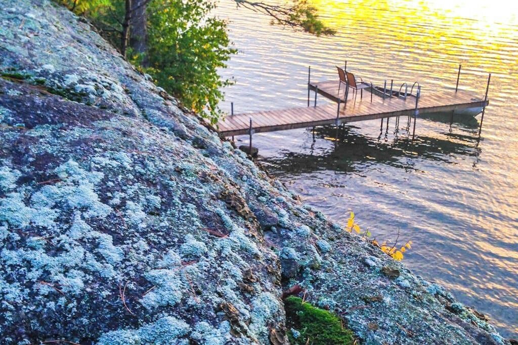 A wooden dock extending into calm water, surrounded by a rocky shoreline with lichen.