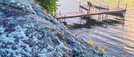 A wooden dock extending into calm water, surrounded by a rocky shoreline with lichen.