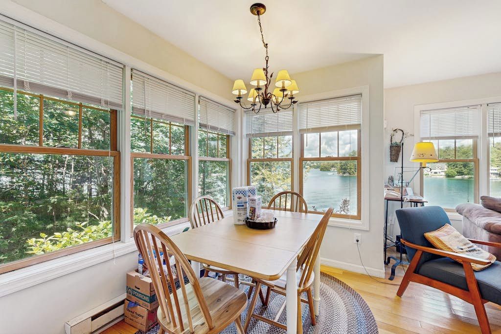 A dining area with a table and chairs, large windows with blinds, a chandelier, and a view of a lake.