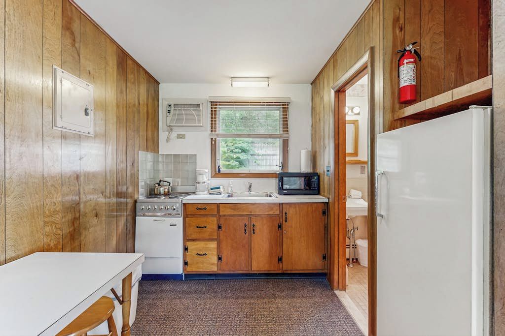 Une cuisine de taille réduite, dotée de meubles de rangement en bois, d’un four à micro-ondes, d’une cuisinière et d’un réfrigérateur.