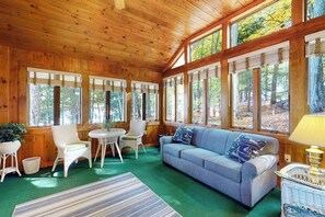A cozy cabin interior with a wooden ceiling, large windows, a blue sofa, and a small round table. - Stunning 1BR Lakefront - Dock - Deck (Moultonborough)