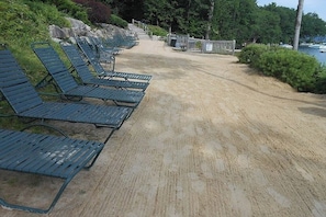 Ein Strand mit Reihen grüner Liegen und einem Sandweg zum Wasser.