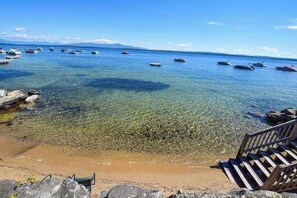 Una playa con aguas cristalinas, barcos y una escalera de madera que baja hacia la orilla.