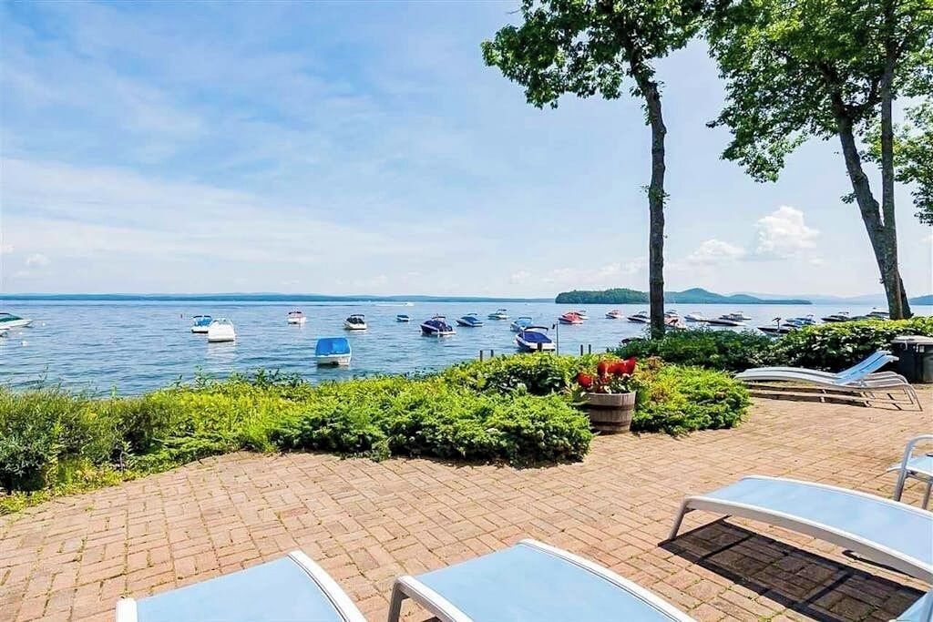 A waterfront patio with lounge chairs, a brick pathway, and boats on the water.