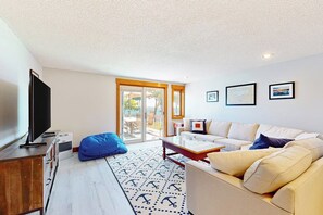 A living room with a sofa, a coffee table, a television, and a patterned rug. - 3BR Samoset Lakefront Townhouse (Gilford)